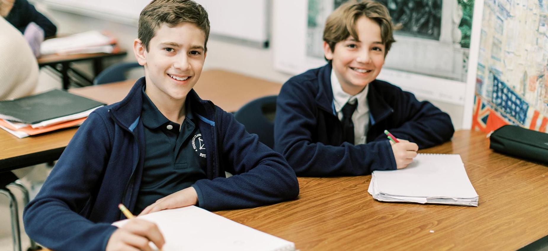 Two smiling middle school boys at their desks during class