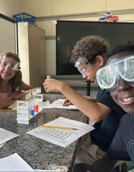 Smiling children in goggles conducting a color-based science experiment at a table.