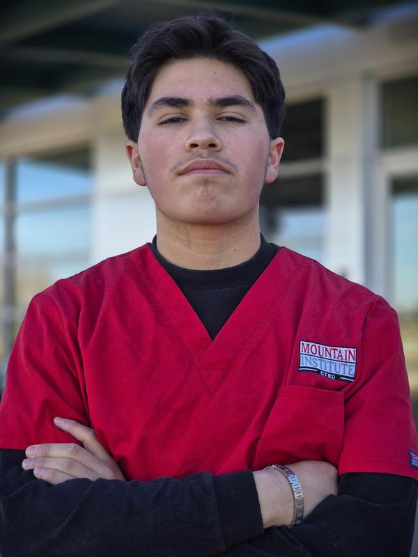 Man in red scrub top with black long sleeve tee underneath looking directly at camera