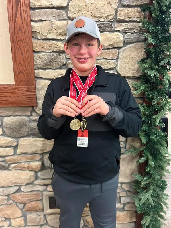boy smiles wearing hat hold two gold medals