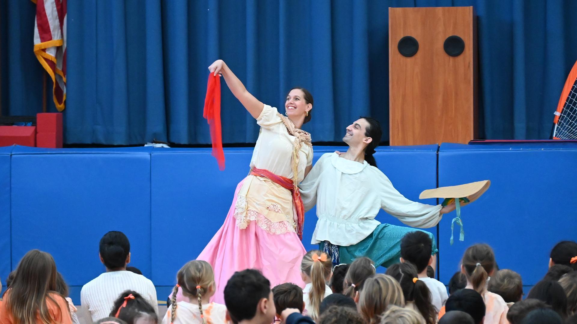 Two performers on stage, one in a pink dress, the other in a light blue shirt, entertaining an audience.