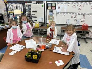four students dressed as doctors working on vowel surgery on table