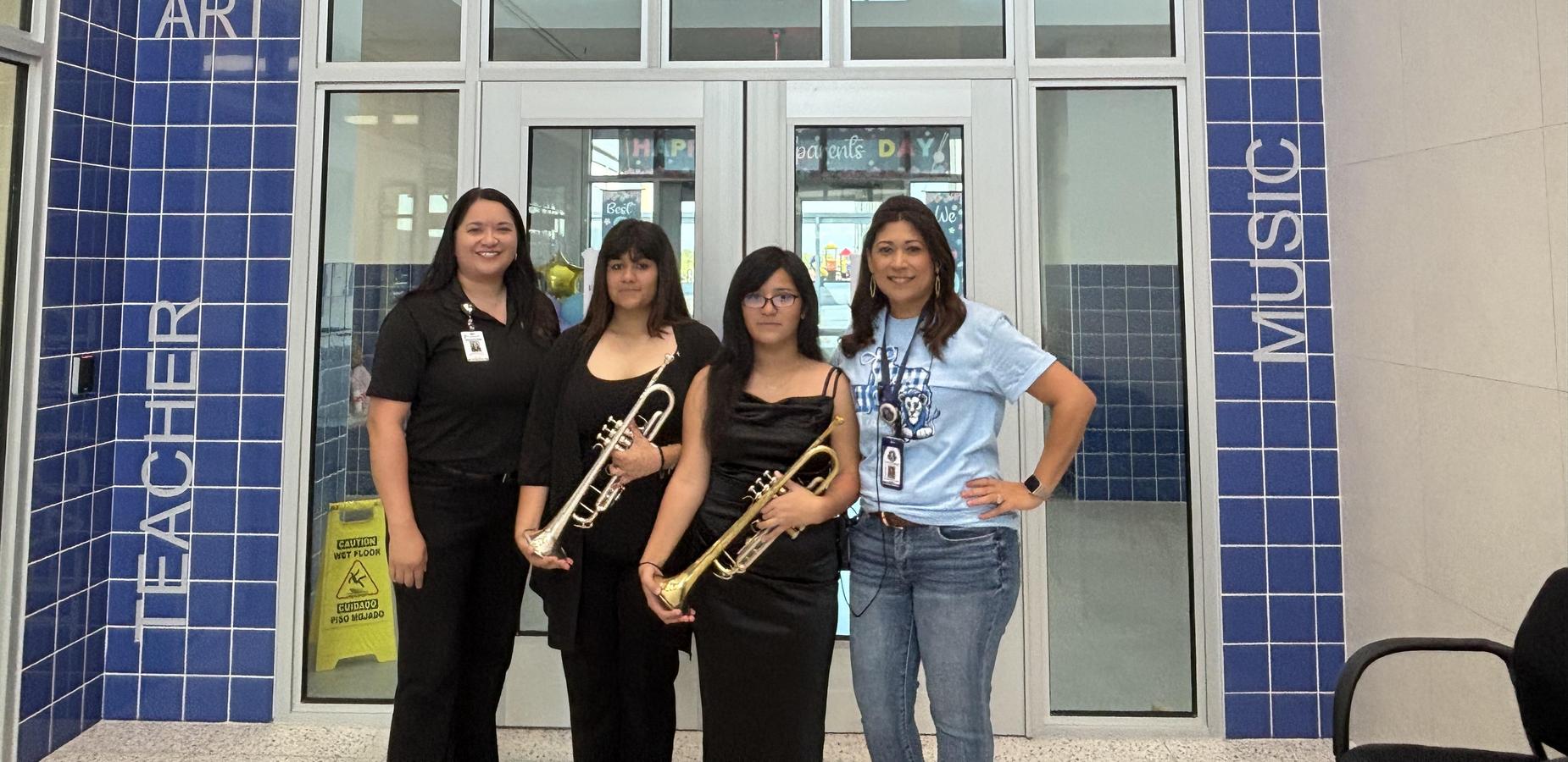 Four people posing with trumpets in a school lobby setting.