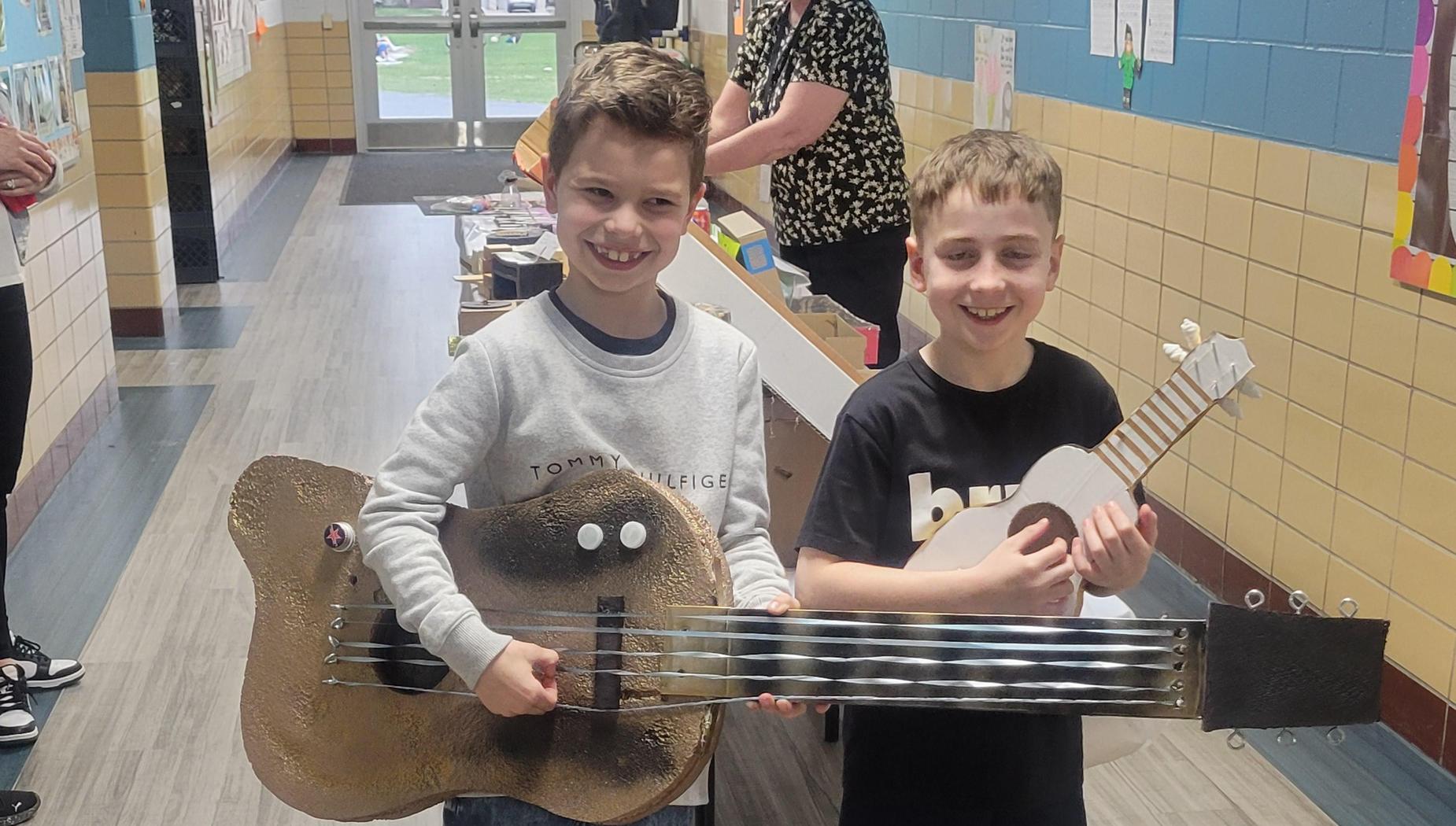 Two children holding large and small musical instruments in a hallway.