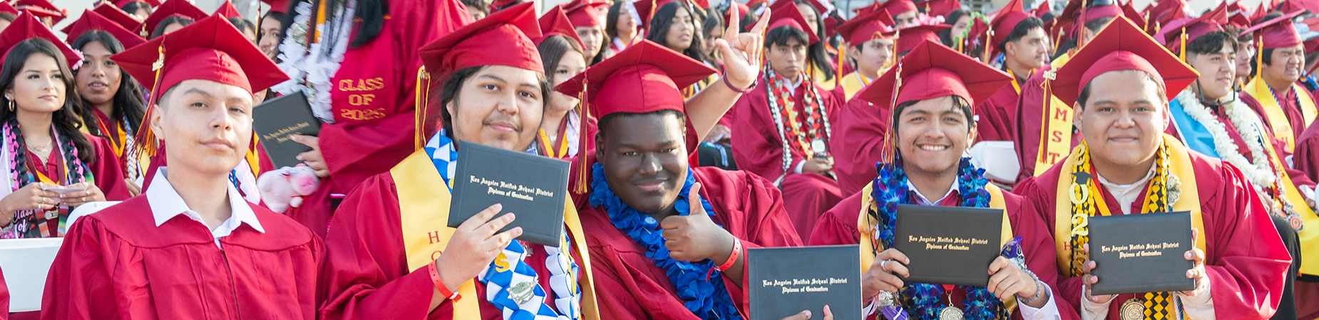 high school graduates wearing red caps and gowns and holding diplomas