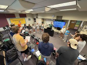 male choral director surrounded by high school chamber ensemble singers