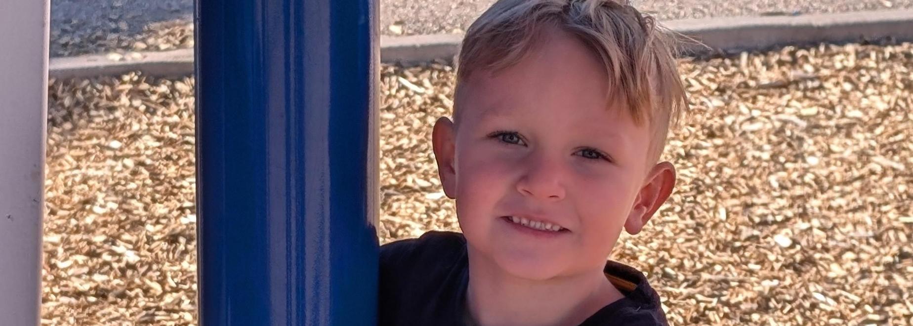 Child hugging a blue pole on wood chips.