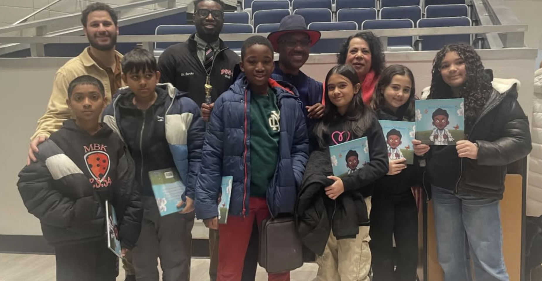 Group of adults and children holding booklets, smiling together indoors.