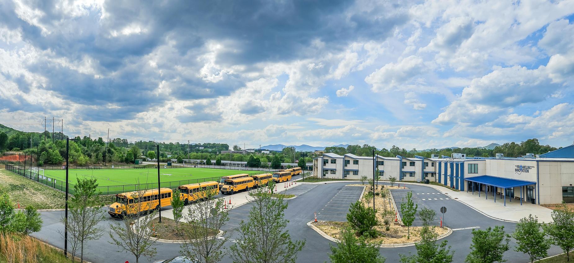 Panoramic image of a school building with a parking lot and an athletic field