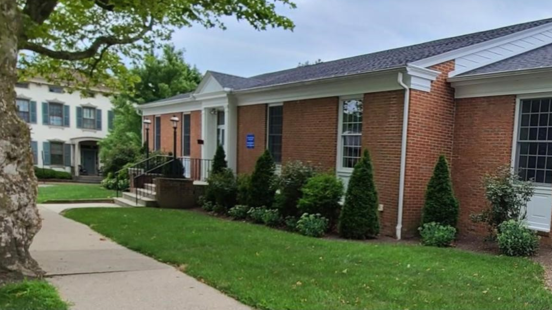 Brick building with white trim, landscaped yard, and sidewalk.