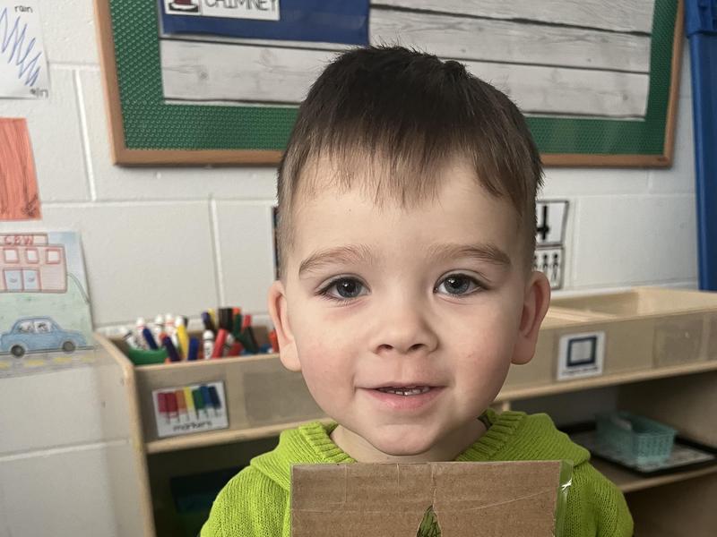 Boy smiling with a cardboard Christmas tree craft decorated with sequins.