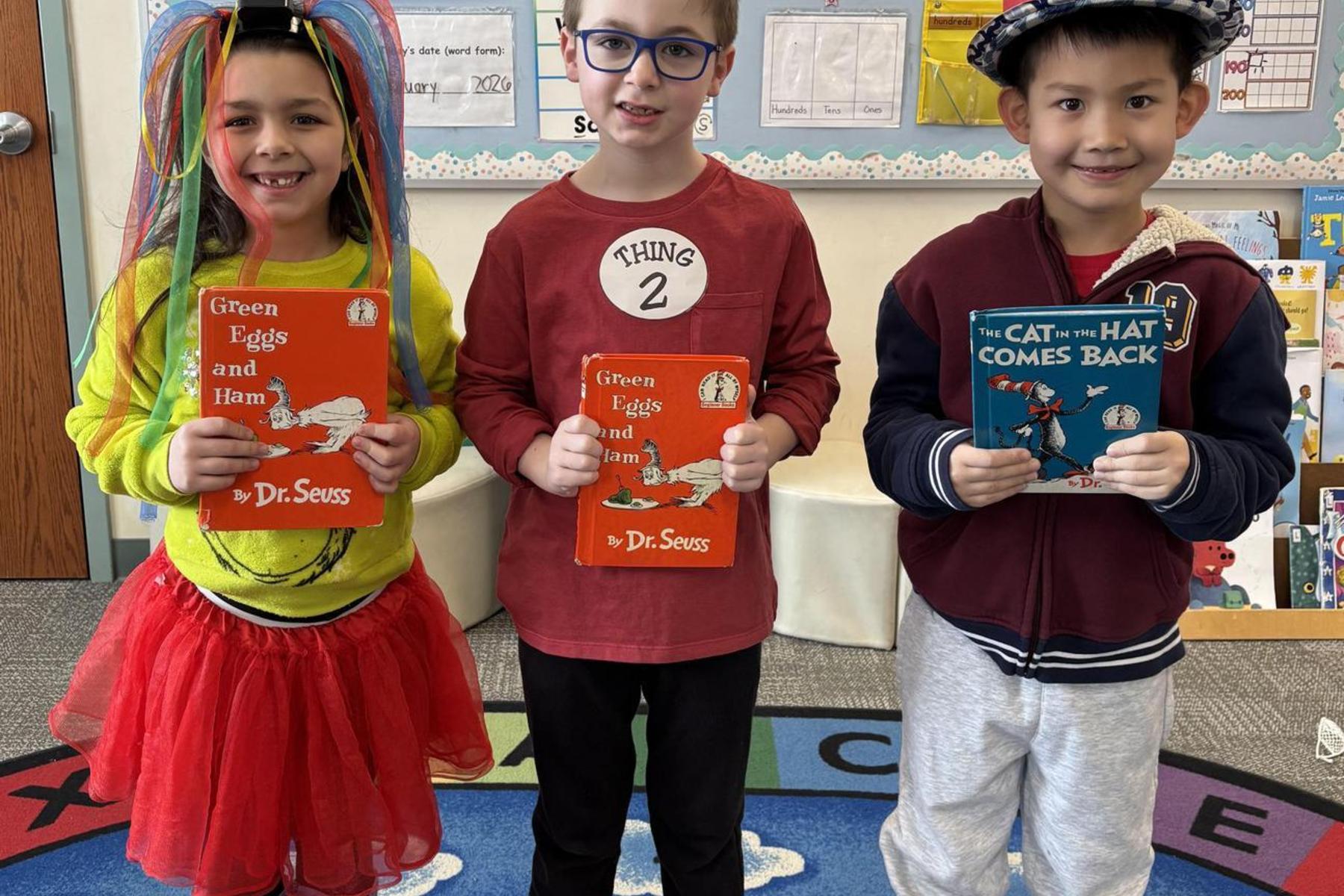 Three children dressed in costumes holding Dr. Seuss books in a classroom.