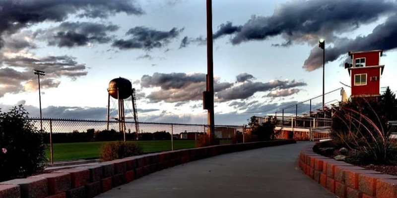 A path leads towards a water tower and an overhead structure under a cloudy sky.