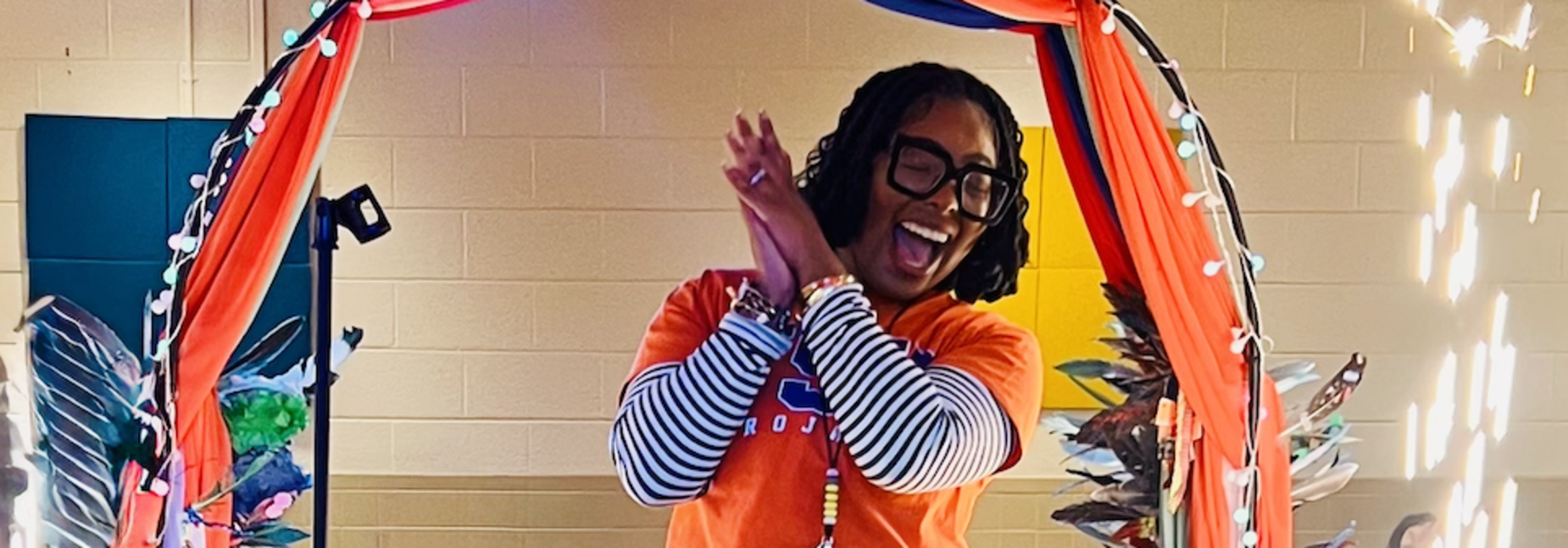 Person taking a selfie in a mirror, wearing an orange shirt and blue jeans.