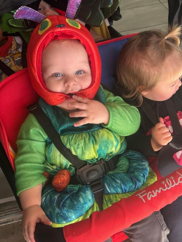 A toddler in a caterpillar costume smiles while sitting in a stroller.