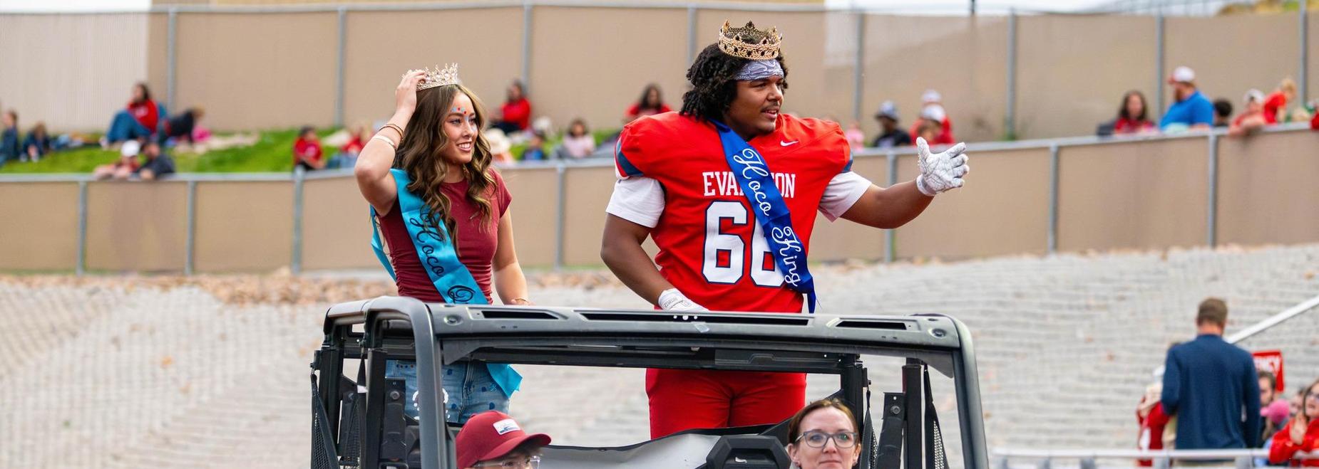 Homecoming royalty on a parade float with fans cheering.