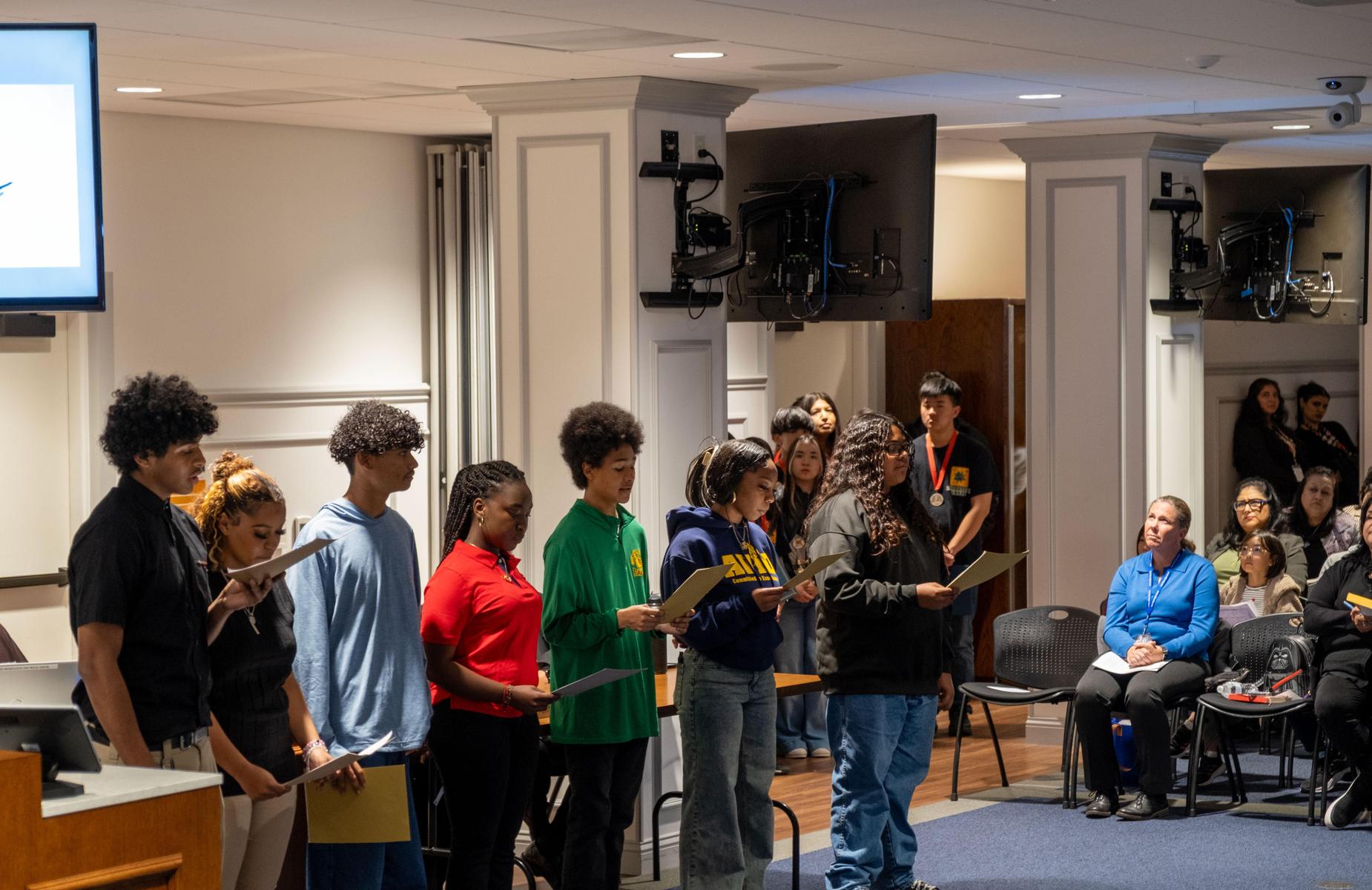 9 persons in school board room pose for photo with students