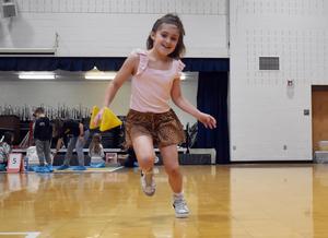 A young girl runs across a gym floor holding a yellow object, wearing a playful outfit.
