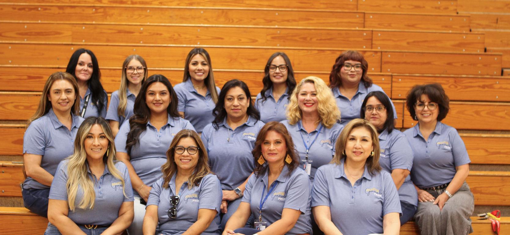 Group of smiling women in blue shirts sitting on bleachers.
