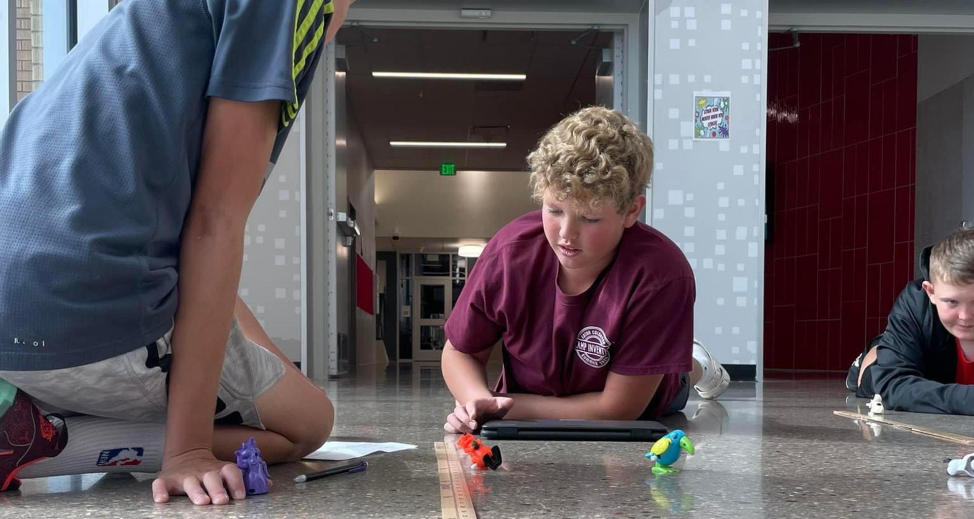 Boys engage in hands-on activities, measuring toy animals on the floor with a ruler.