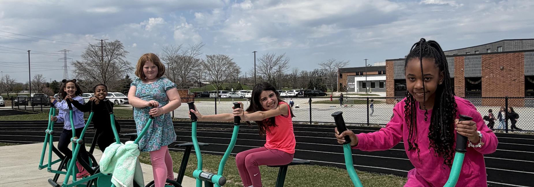 Five girls exercising on outdoor gym equipment at a park.