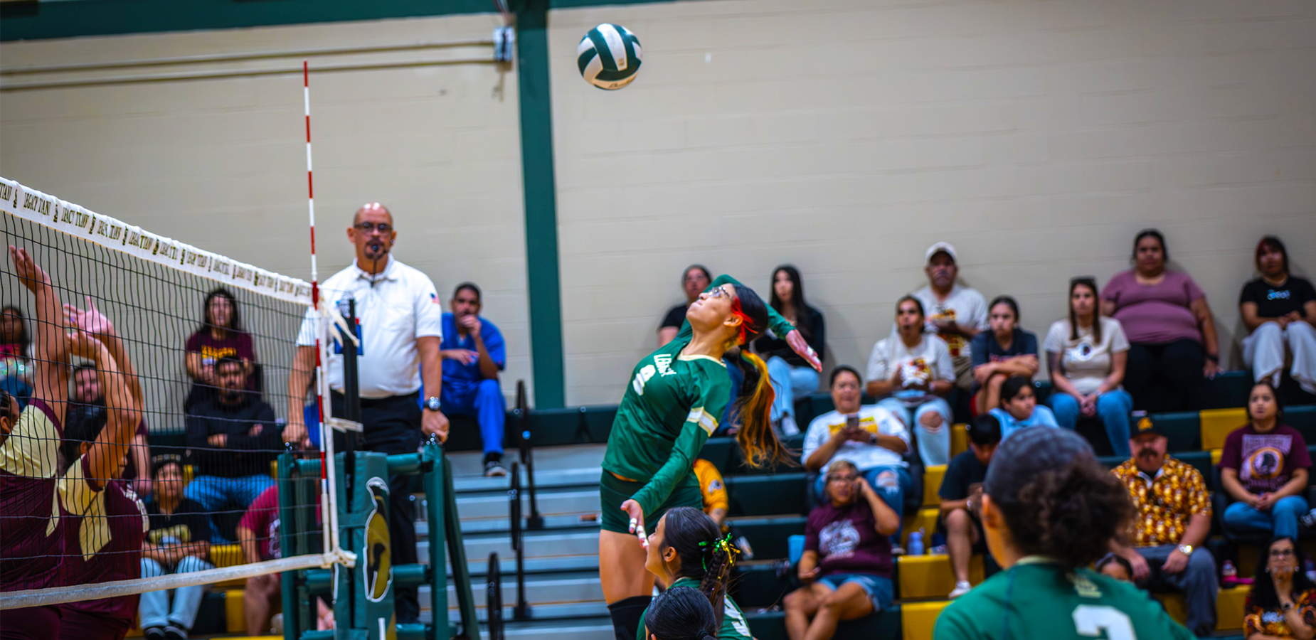 A volleyball player leaps to spike the ball while spectators watch in the background.