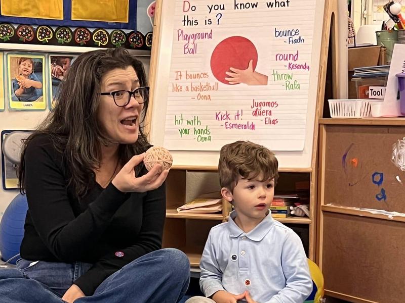 A woman holds a small ball while sitting beside a young boy in a classroom setting.