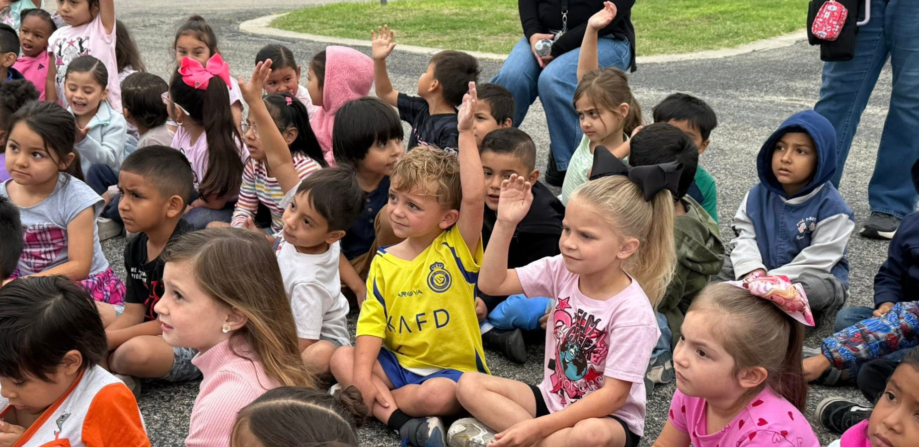 students sitting on blacktop raising their hands