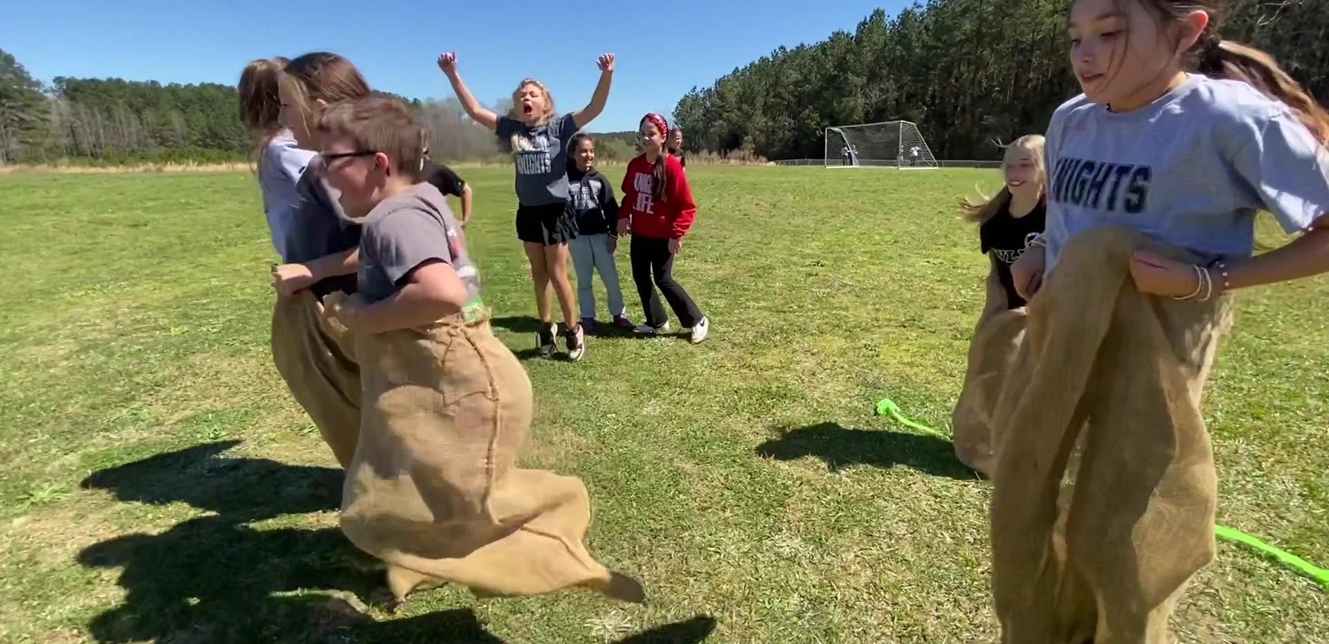 Students participating in a sack race on a grassy field.