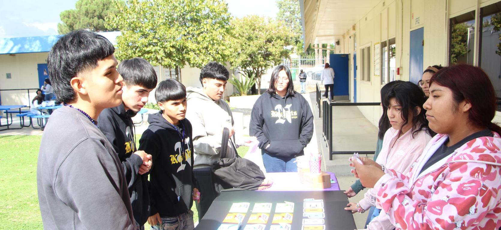 Group of students engaged in a discussion around a table outdoors.