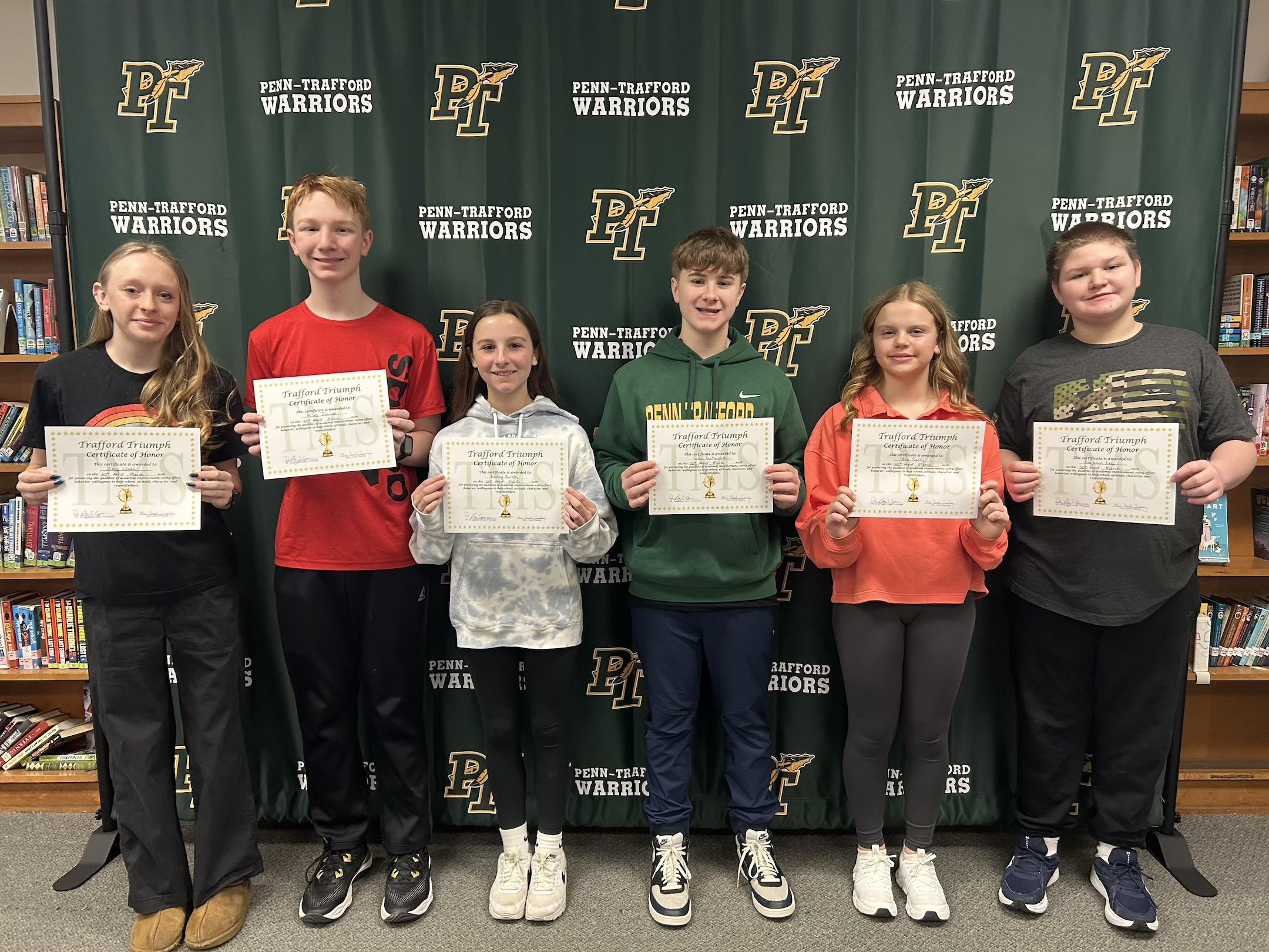 Trafford Triumphs honorees hold their certificates while standing in front of at PT Warrior backdrop