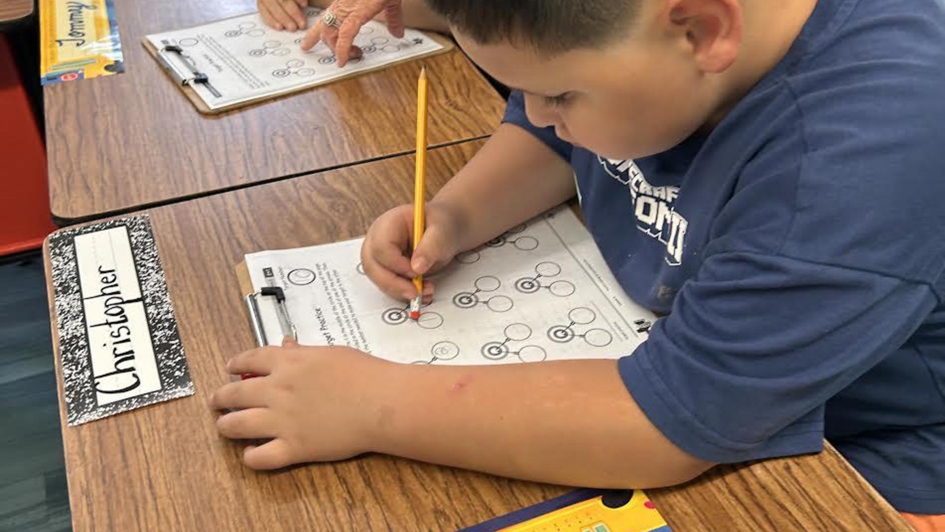 A child sitting at a table, working on a worksheet with a pencil.