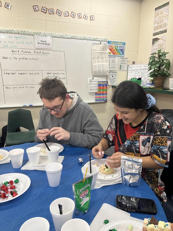 Two students working on their dessert creations with cups and snacks nearby.