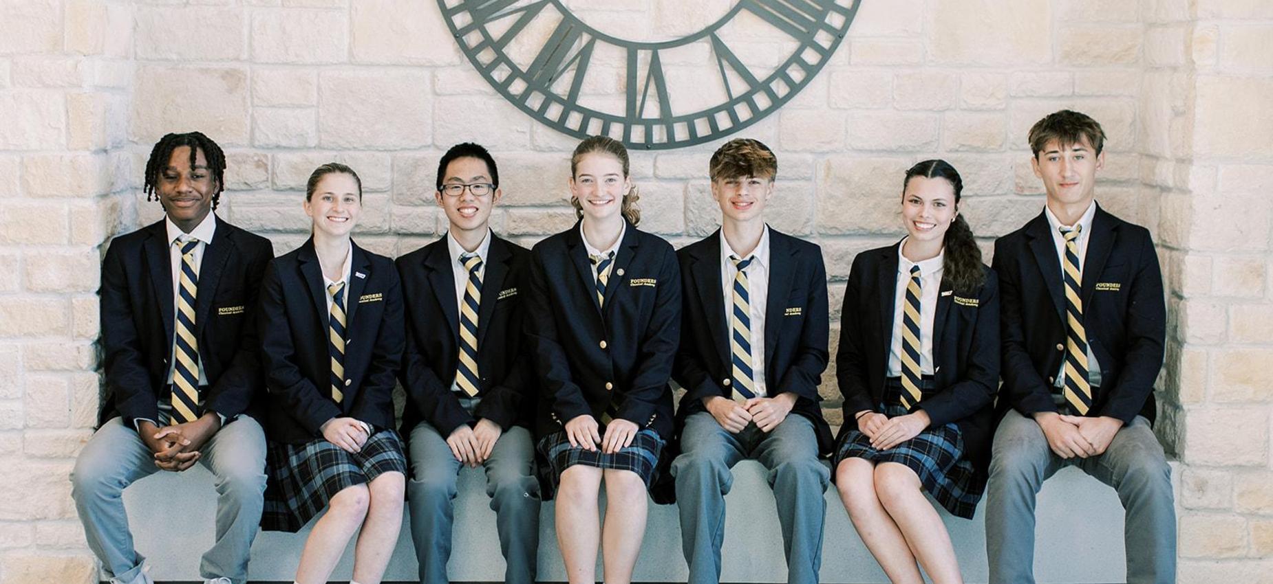High school students in blazers sit together on a bench beneath a large clock