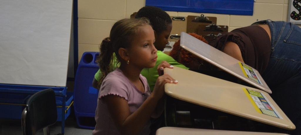 2 students arrange school supplies inside their new desks