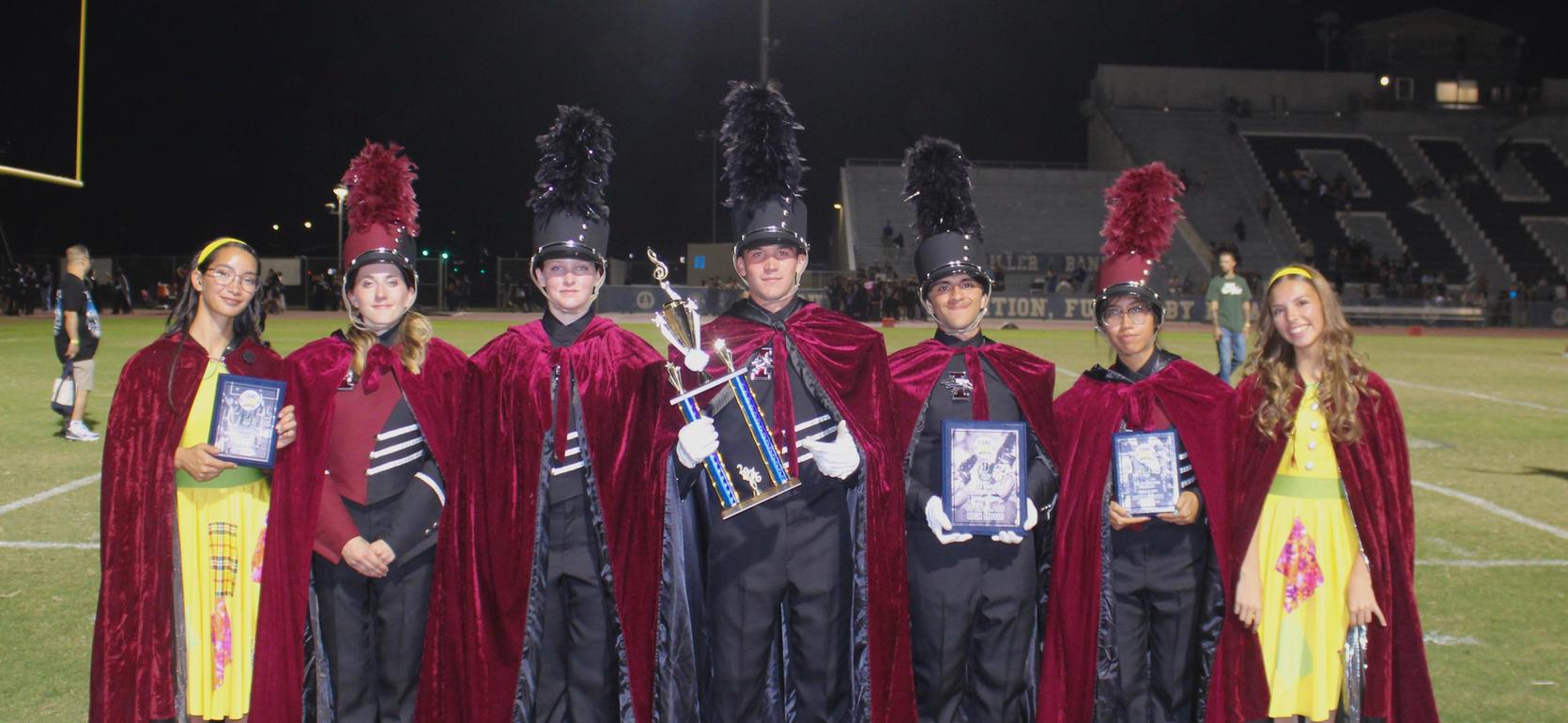 Group of students in capes holding awards on a football field.