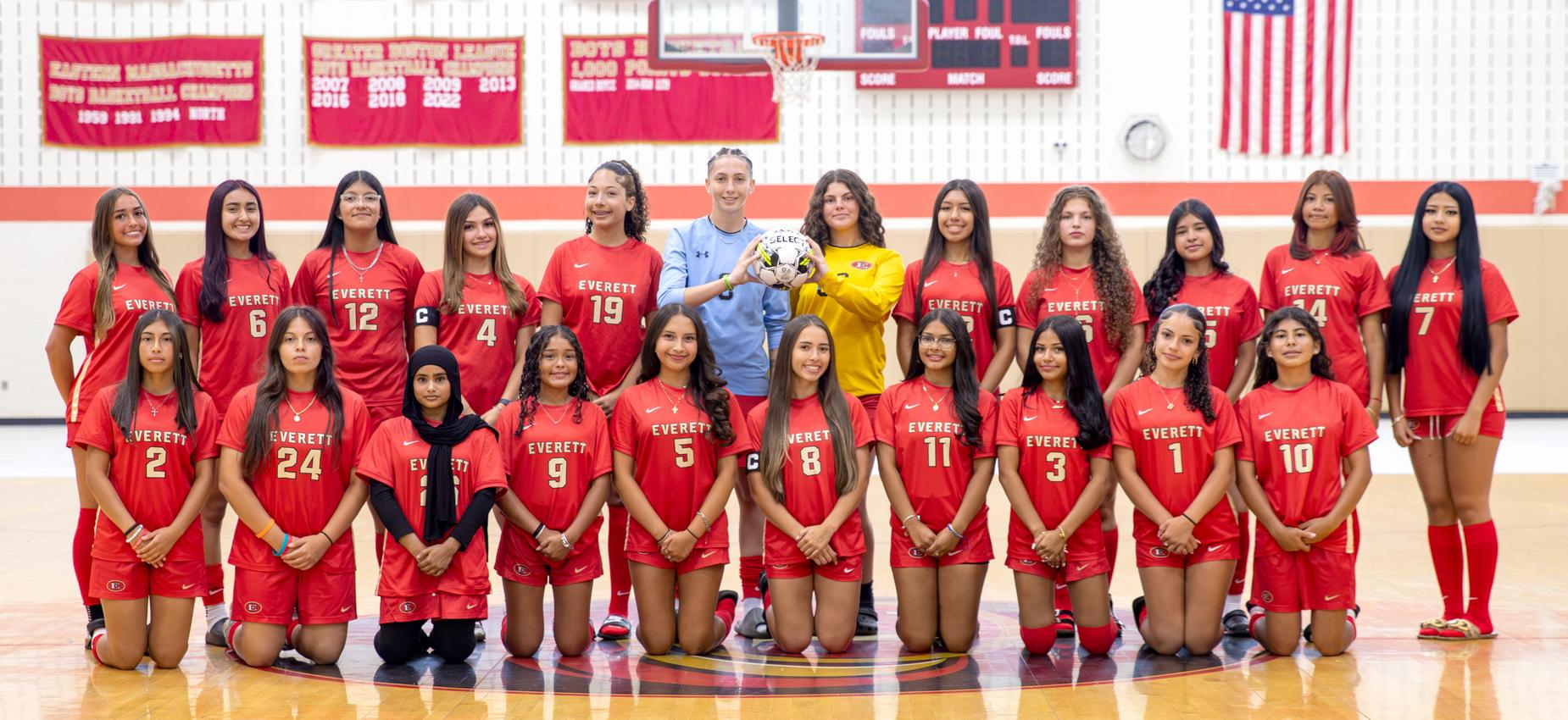 Group of soccer players in red uniforms posing for a team photo in a gym.