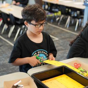 boy cutting bright yellow paper to make a helicopter