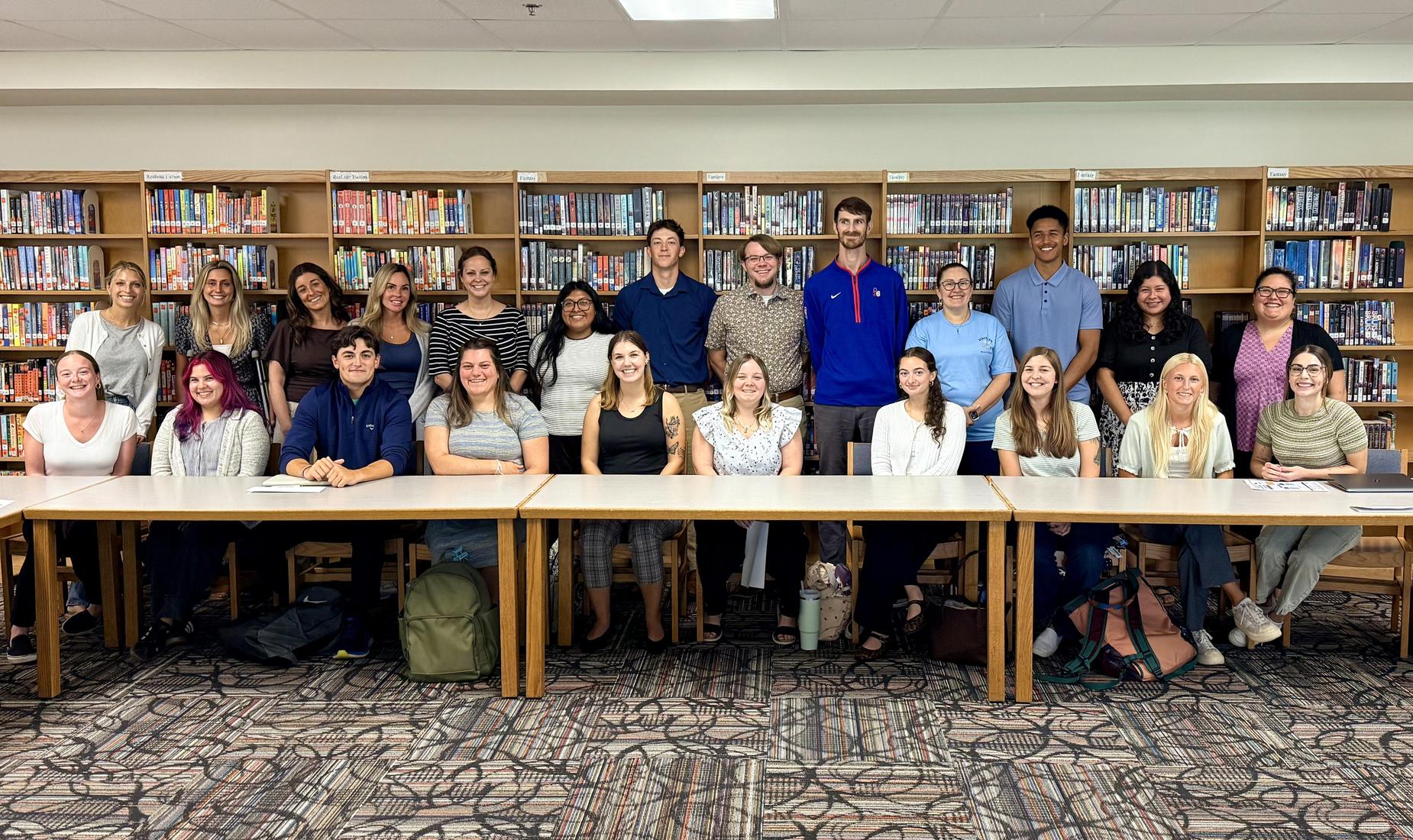 A group of students and teachers posing together in a library setting.