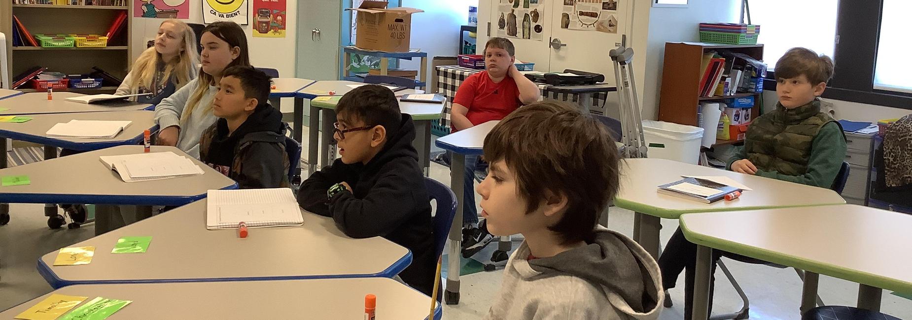 A classroom with several students attentively listening to a lesson at their desks.