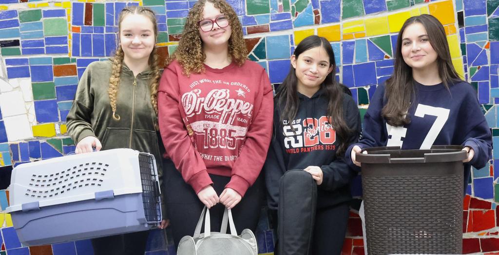 Four girls standing against a wall. One is holding a pet carrier.