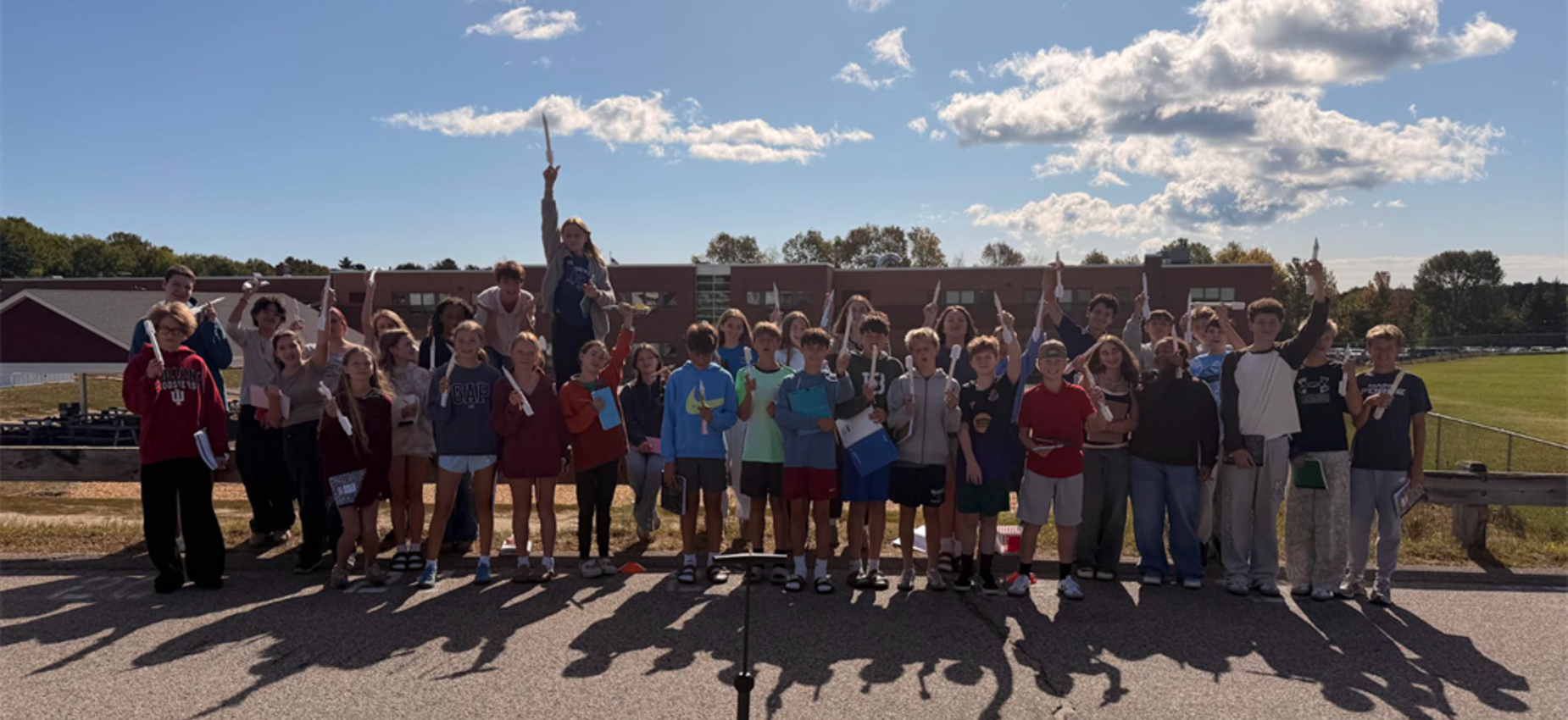A large group of children and adults celebrating outdoors, many with hands raised.
