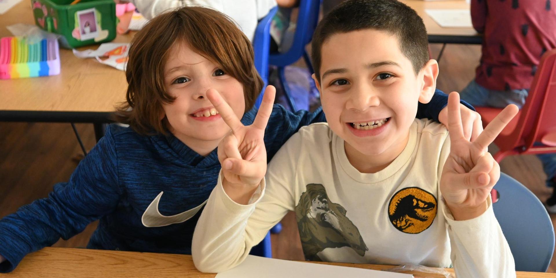 Two children smiling and making peace signs at a table.