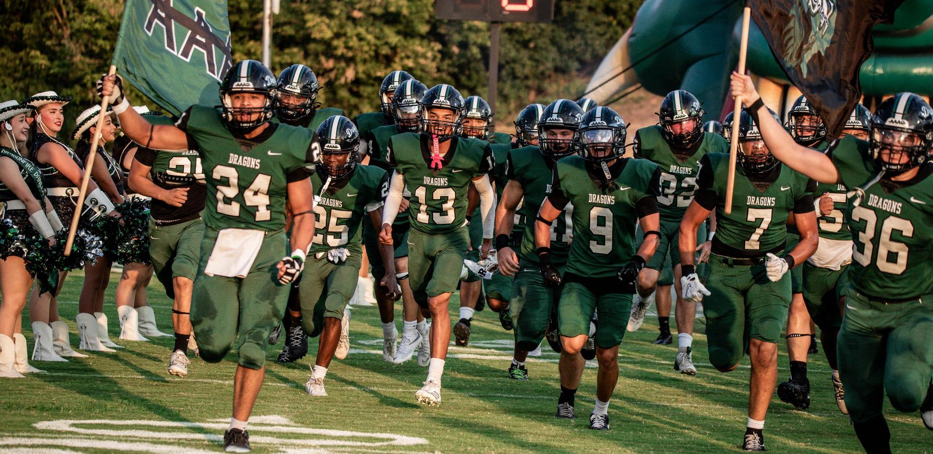 Football players in green uniforms run onto the field with flags and cheering fans.
