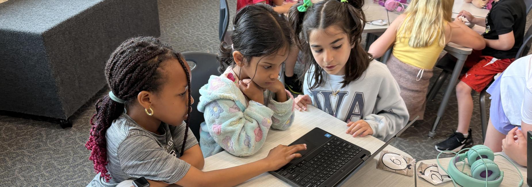 Three children collaborating at a table with a laptop and headphones.