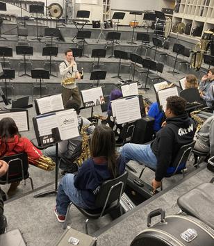 Students in a music room practicing with a conductor leading the rehearsal.