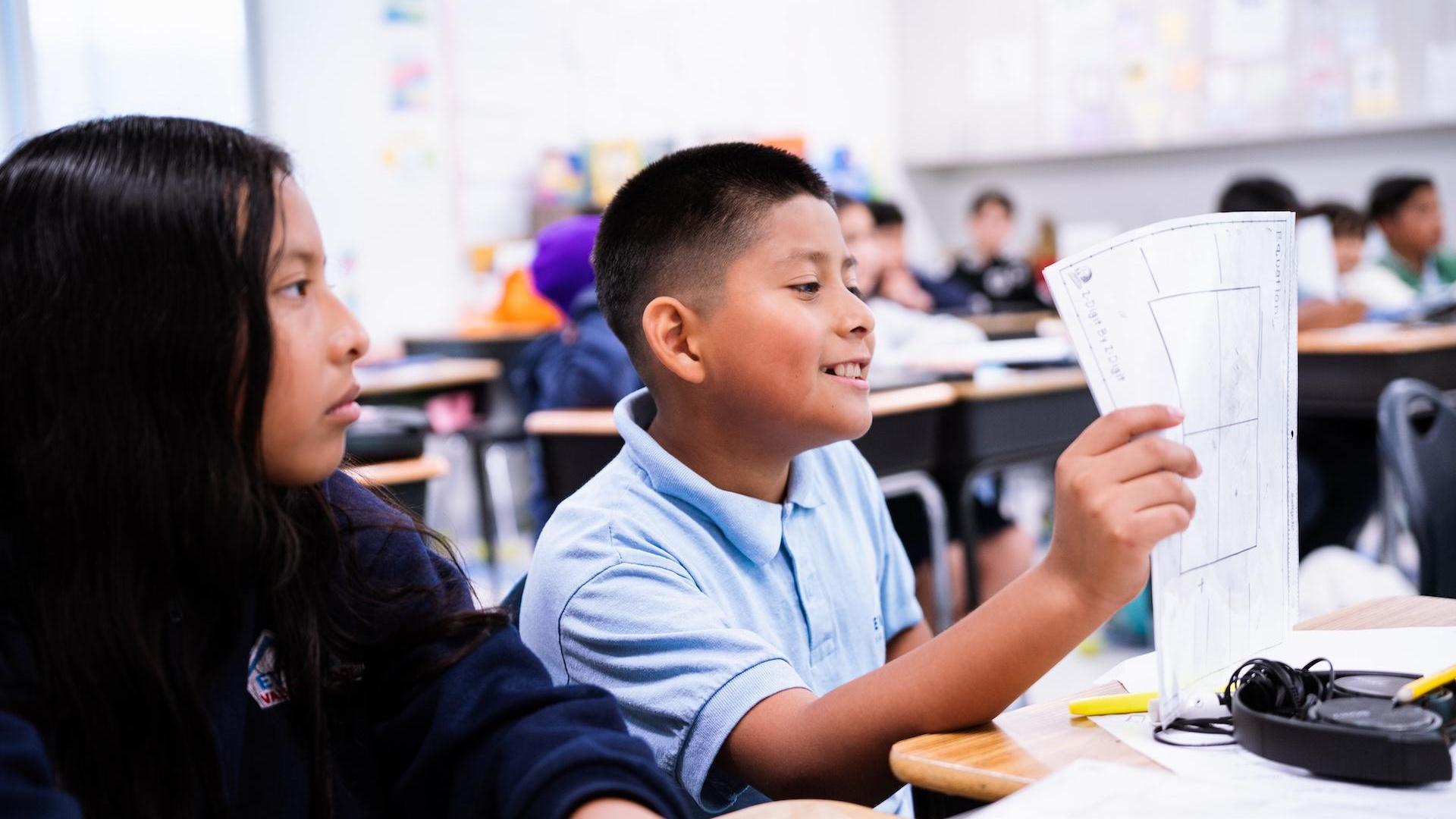 A boy showing a paper to a girl in a classroom.