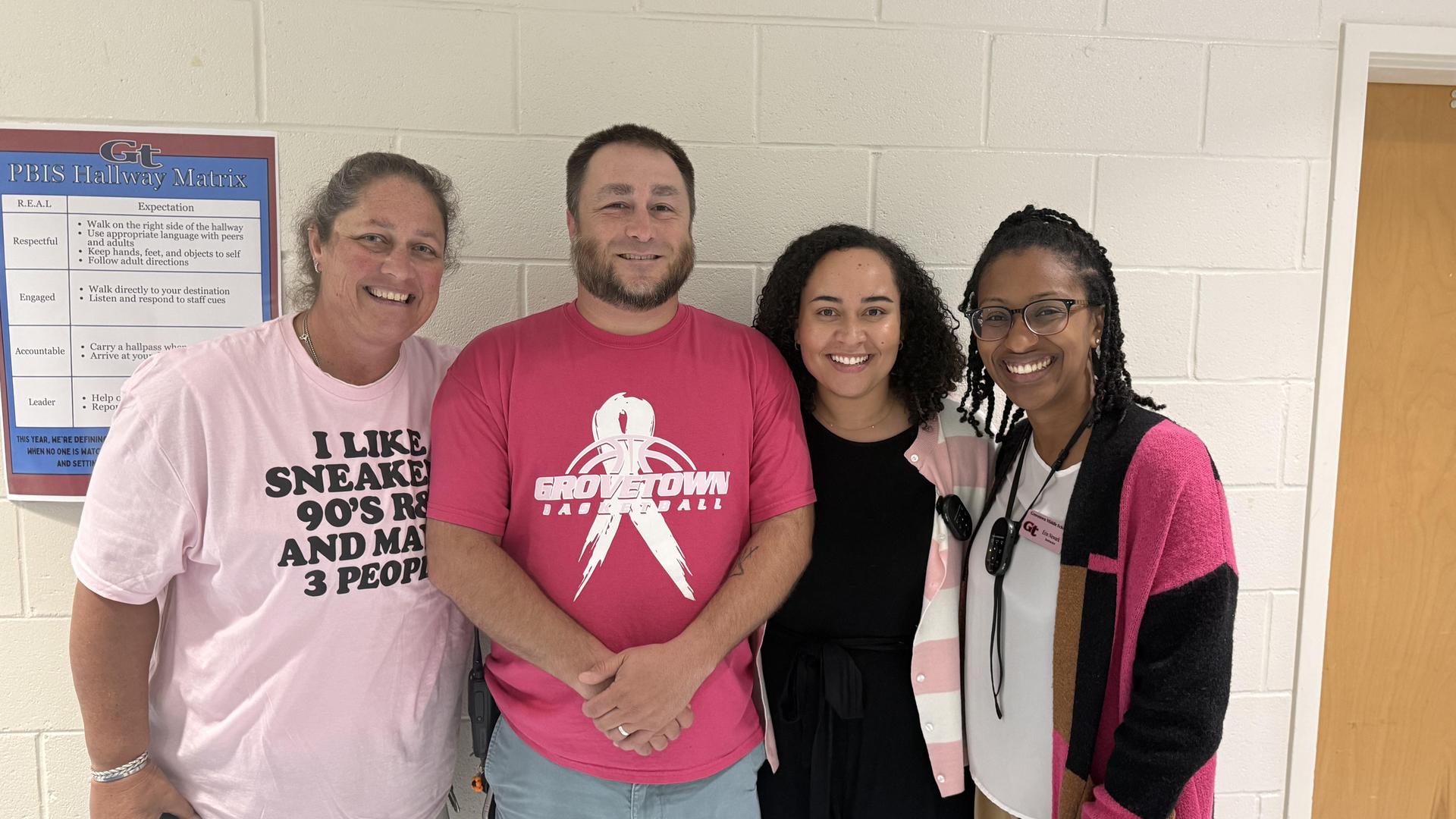 Four people posing together, smiling, in a hallway setting.