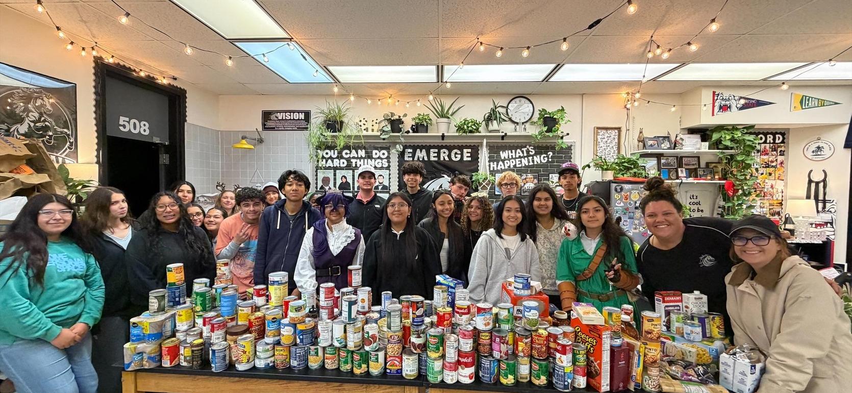 Group of students and adults posing with food donations in a decorated room.