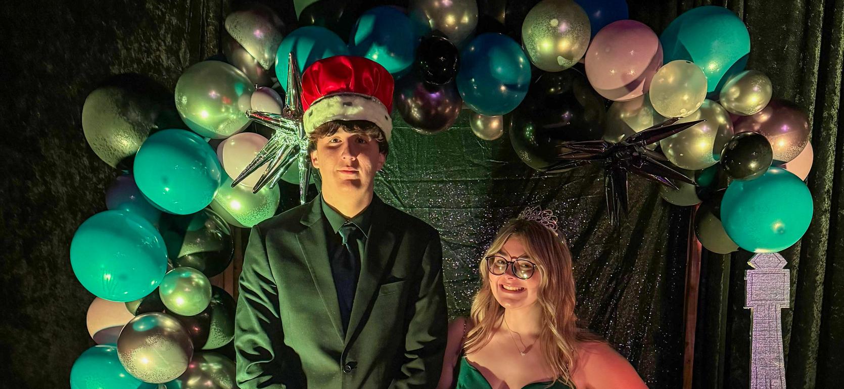 Two people posing together in formal attire with a decorative backdrop.